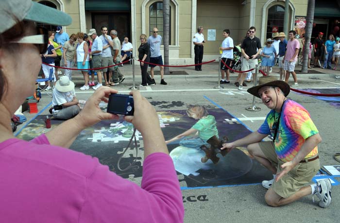 A A lady in a pink shirt photographs a tie-dyed guy with the puzzle piece